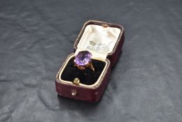 An amethyst ring of oversized oval form in an eight claw basket mount on a yellow metal loop stamped
