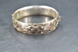 A silver hinged bangle having engraved floral decoration