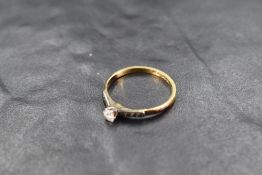 A diamond solitaire ring, approx 0.128ct in a claw set mount to moulded shoulders on a yellow
