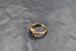 An early 20th century ring having a blue paste gem in a collared mount on a yellow metal loop