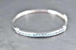 A 9ct white gold hinged bracelet having eighteen blue topaz style stones in a channel setting with a