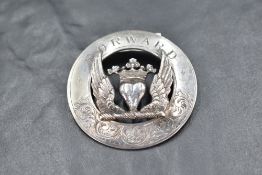 A white metal garter or kilt pin, of circular form with crowned heart between wings, the surround