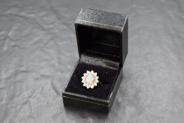 A 9ct gold opal and diamond flower-head cluster ring, the central raised oval opal within a band