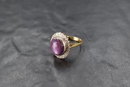 An Amethyst oval cabochon ring having a diamond chip surround and possible asterism on a yellow
