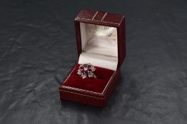 A multi cluster ring having a central diamond surrounded by six oval rubies in petal form within a