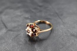 A garnet and seed pearl triple daisy cluster in a raised claw set mount on a 9ct gold loop, size M &