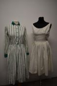 Two vintage 1950s day dresses, one cream with pleated skirt and the other white cotton with green