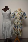 Two 1950s day dresses, one having V neckline, pleated skirt and abstract floral pattern, the other