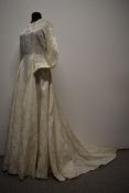A 1950's wedding dress in cream, having long sleeves, full skirt and pearlescent buttons to nape.