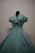 A 1950s textured cotton day dress in aqua blue, with faux buttons to front and cuffs and bow to und