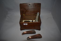A vintage oak box housing a collection of vintage shoe horns, having advertising for Manchester