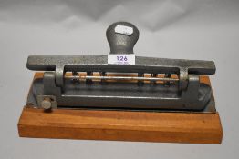 A large vintage desk top hole punch, mounted on wood block.