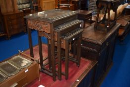 An Oriental nest of three tables with carvings to frieze and under glass to top