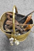 A brass coal bucket containing various fire side tools, horse shoes and a flat iron.