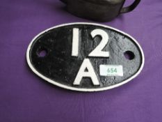A cast metal oval Shed Plate 12A (Carlisle) in black with white numbering and border, 19cm x 12cm