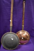 Two antique copper bed warming pans with turned wood handles.