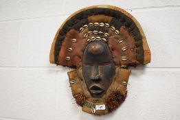 An early 20th century African Dan tribal ritual mask adorned with woven surround and sea shells