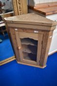 A stripped pine corner wall cupboard having glazed door