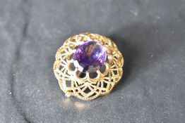 A 1960's amethyst brooch having a central oval stone within a decorative moulded pierced mount,