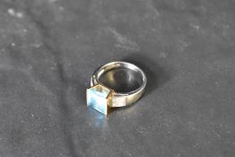 A blue topaz solitaire ring of stylised form, having a tension set princess cut convex stone in a
