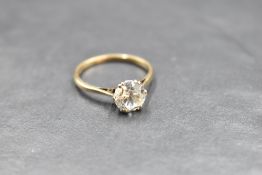 A solitaire ring bearing a clear stone, not a diamond in a raised claw set mount on a yellow metal
