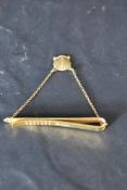 A 9ct gold tie slide of plain form bearing a chain drop to a 9ct gold scallop shell charm for 25year