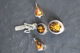 Three pieces of amber style jewellery having carved floral decoration in white metal mounts, no