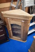 A stripped pine corner wall cupboard having glazed door