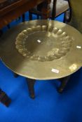 An Oriental tray table having brass top and carved folding frame