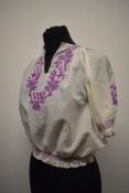A vintage peasant blouse, having purple hued embroidery, smocking to sleeves and hem and