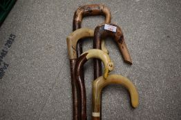 A collection of 5 crooked walking sticks of varying lengths one of which is carved into the shape of