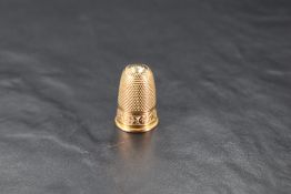 A yellow metal thimble, of traditional design with shield form cartouche and foliate band, unmarked,