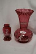 Two Mary Gregory style cranberry glass vases, the largest having a flared and crimped rim, measuring