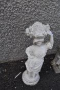 A concrete garden ornament, girl with fruit basket aloft