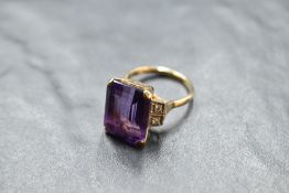 An art deco style baguette cut amethyst ring having diamond set shoulders on a yellow metal loop