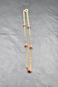 A yellow metal chain bearing plaque stamped 9ct having five coral beads spaced within the chain,