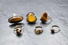 Six silver and white metal rings of various forms, including Tiger's Eye and Baltic Amber