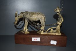 An Indonesian depiction of a man working the fields in brass sat on mahogany base.