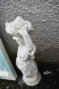A concrete garden ornament, girl with fruit basket aloft