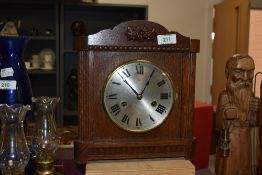 An early 20th Century oak cased mantel clock, the shaped pediment above a silvered Roman dial,