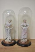 A pair of 19th century German bisque porcelain figures under glass domes.