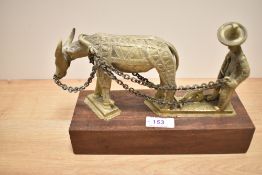 An Indonesian cast brass depiction of a man working the fields sat on mahogany base.