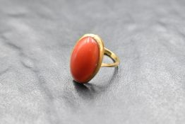 An oval coral cabochon set ring in a collared mount on a yellow metal loop stamped 750, size L &