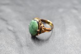 An oval jade cabochon ring in a four claw collared mount on a Chinese gold loop, size K and approx