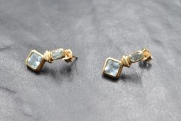 A pair of 9ct gold earrings having baguette cut collared aquamarine studs with gold drops to further