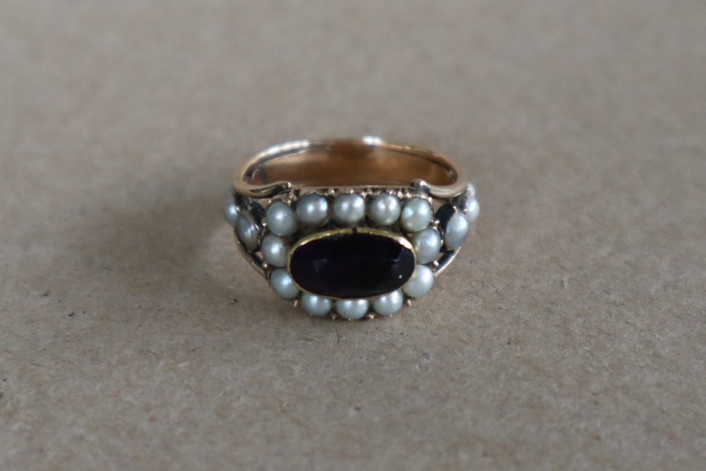 A late George III mourning ring set with a central oval faceted amethyst surrounded by half section