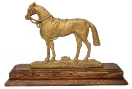 A gold painted cast metal figure of a horse mounted on an oak plinth base