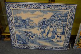 A blue and white porcelain tile picture depicting a man on horseback with hounds.