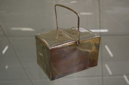 A silver twin compartment box with pair of hinged covers and a swing handle.