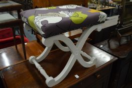 A painted X frame stool with abstract upholstery.